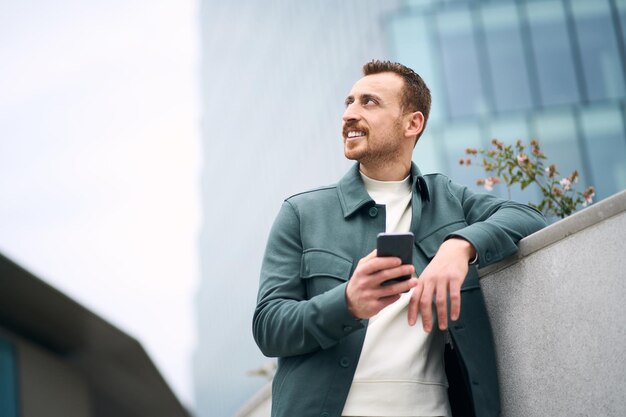 Smiling man using mobile phone shopping online looking away on\
the street, copy space