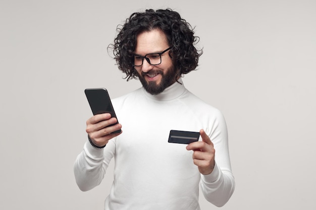 Фото Улыбающийся мужчина использует пластиковую карту и смартфон для покупок в интернете