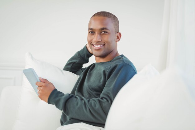 Smiling man using tablet on the sofa and looking at the camera