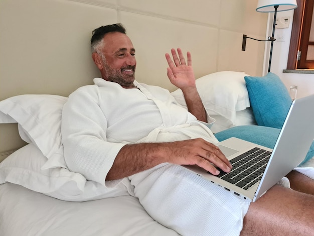 Улыбающийся мужчина машет видеозвонком через ноутбук дома или в отеле