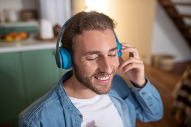 A smiling man wearing blue earphones while listening to music