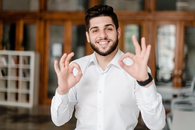 Smiling man in white shirt showing ok gesture in the office