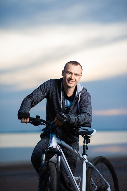 Photo smiling man with bicycle on the beach during sunset