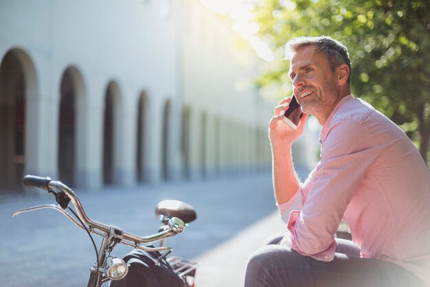 Smiling man with bicycle on the phone on a park bench