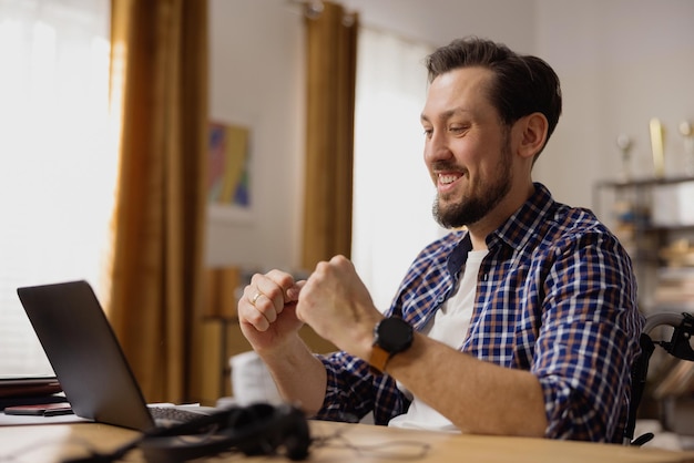 A smiling man with a disability sits in front of a laptop enjoying doing a project assigned to him