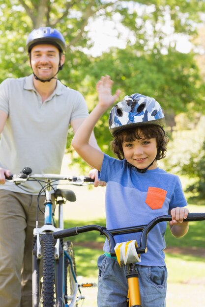 Улыбающийся человек со своим сыном, катаясь на велосипедах