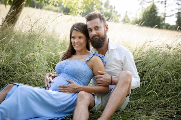 Photo smiling man with pregnant woman in meadow