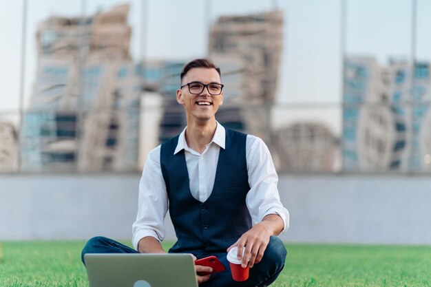 Photo smiling man with a takeaway coffee talking on his smartphone in front of a business center