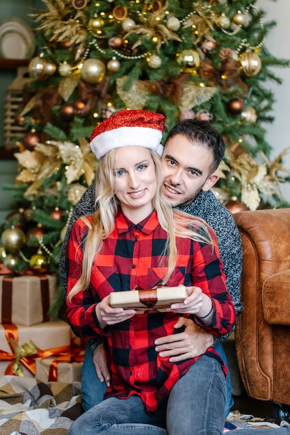 Uomo e donna sorridenti che abbracciano e che tengono il contenitore di regalo, presentandosi i regali di natale l'un l'altro, celebrando le vacanze invernali