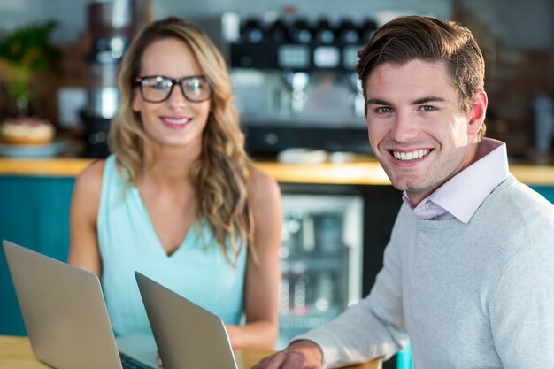 Smiling man and woman using laptop in cafe