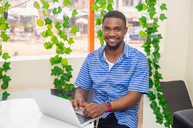 Smiling man working on laptop in a bright office with hanging plants