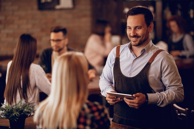 Uomo sorridente che lavora part-time come cameriere e prende l'ordine da un ospite femminile in un bar