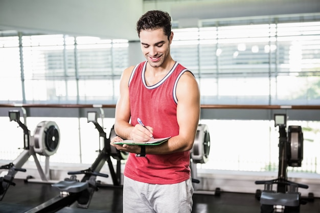 Smiling man writing on clipboard in the gym