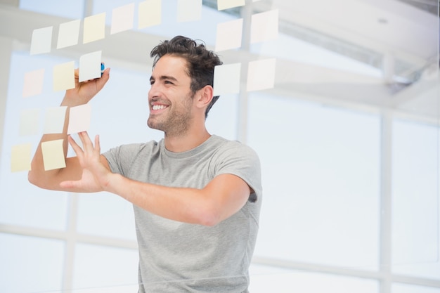 Smiling man writing on sticky notes on window