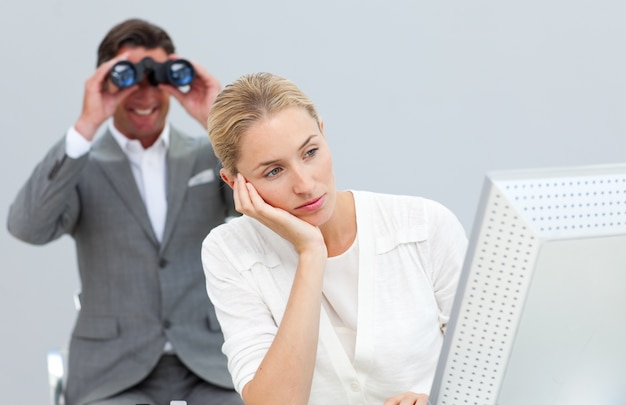 Smiling manager holding binoculars looking at his colleague's computer