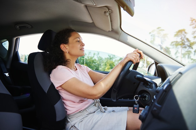 Photo smiling mature african american ethnicity woman sitting on a driver seat and putting her hands on the steering wheel