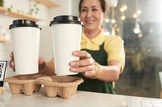 Smiling mature barista putting two cups of take out coffee in holder