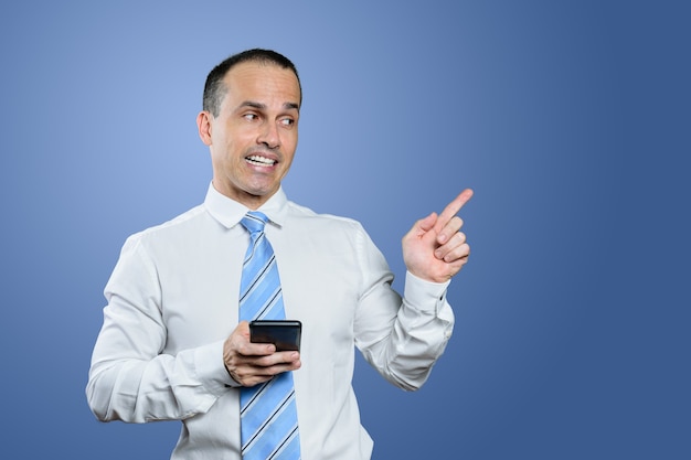 Smiling mature Brazilian man in formal wear and pointing his finger to his left. Blue background.