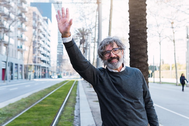 Foto un uomo d'affari maturo sorridente in piedi per strada in città alza la mano per chiamare un taxi