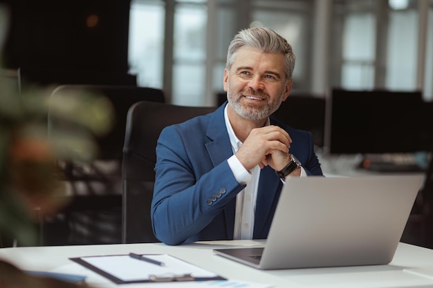 Smiling Mature businessman workingon laptop while sitting in modern coworking