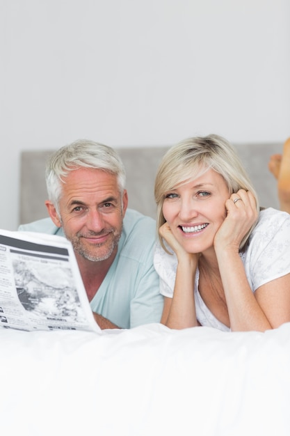 Photo smiling mature couple reading newspaper in bed