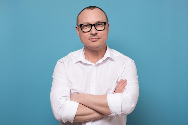 Photo smiling mature man in glasses and white shirt standing with folded hands