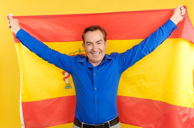 Улыбающийся зрелый мужчина поднимает испанский флаг