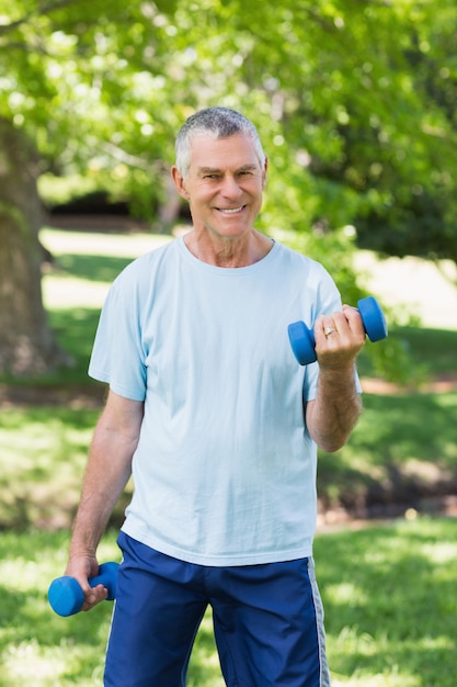 Uomo maturo sorridente con manubri al parco