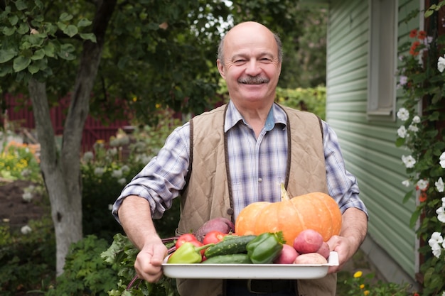 彼の庭で採れた野菜を持つ成熟した男の笑みを浮かべてください。
