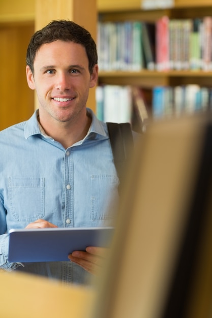 Foto studente maturo sorridente con il pc della compressa in biblioteca