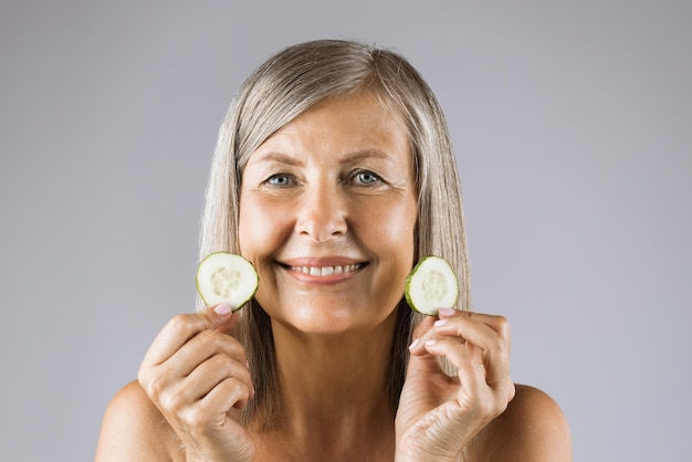 Smiling mature woman holding slices of fresh cucumber