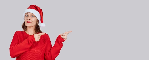 Улыбающаяся зрелая женщина в новогодней шапочке, красном свитере показывает место для текста.