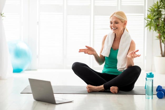 Smiling mature woman in sportswear having online fitness training with laptop at home