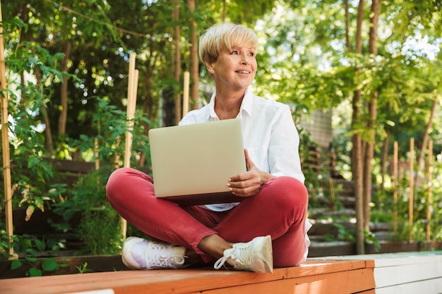 Donna matura sorridente che per mezzo del computer portatile