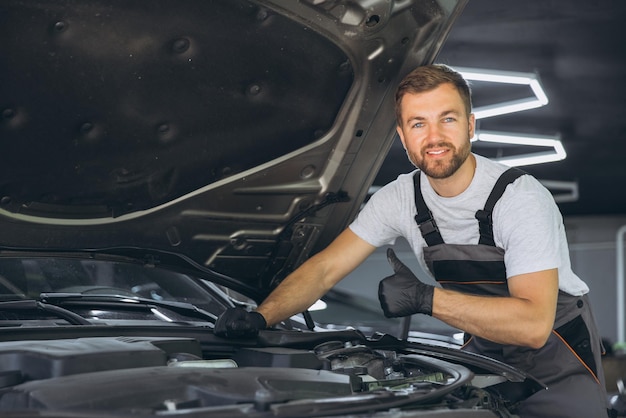 smiling mechanic giving thumbs up while working on car engine in auto repair shop