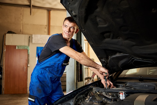 A smiling mechanic is repairing a black car