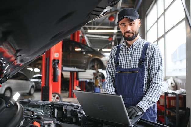 Foto meccanico sorridente utilizzando un pc portatile presso il garage di riparazione