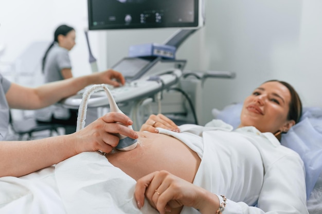 Foto procedura medica sorridente la donna incinta è sdraiata in ospedale il dottore fa l'ecografia