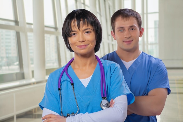 Smiling medical team man and woman with crossed arms looking at camera in modern hospital