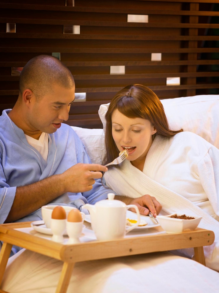 Photo smiling mid adult man feeding girlfriend on bed at home