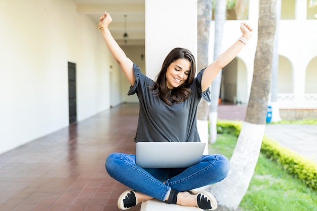 Smiling mid adult woman stretching while using laptop computer at campus