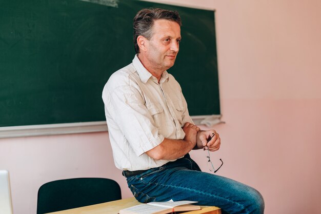 Smiling middle age teacher sitting at the table and explain the lesson .