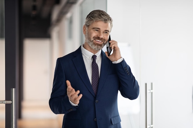Uomo d'affari di mezza età sorridente che parla sul cellulare mentre si cammina fuori dall'ufficio