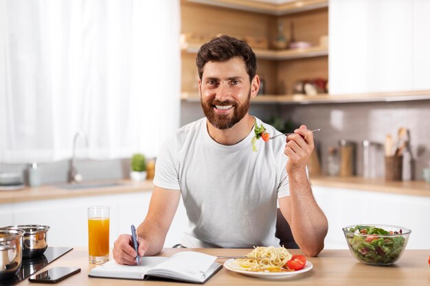 ビジネスを計画し、パスタを食べてメモを作る笑顔の中年ヨーロッパのひげを生やした男