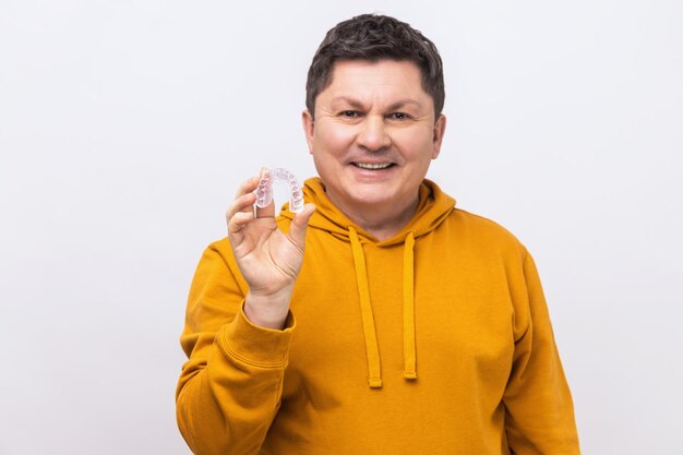 Smiling middle aged man with dark hair holding transparent plastic braces mouth guard