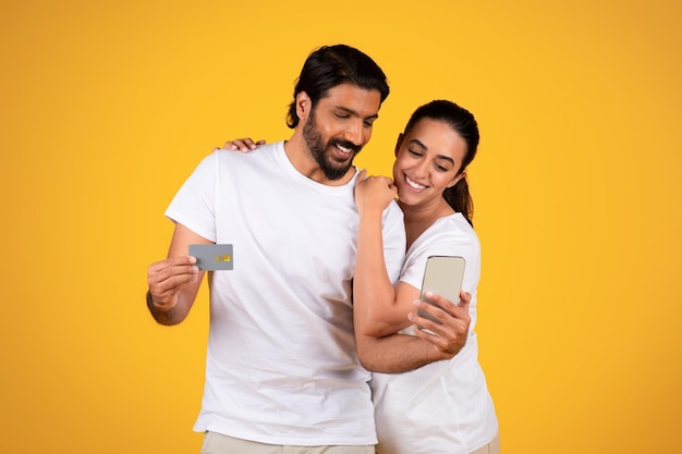 Smiling middle aged mature couple hold credit card and smartphone