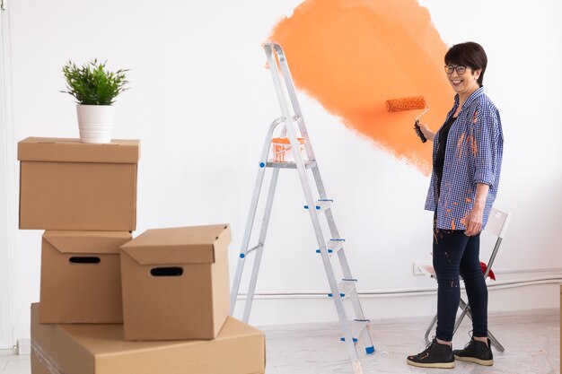 Smiling middle-aged woman painting interior wall of home. Renovation, repair and redecoration