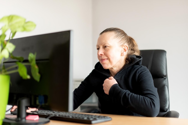 Smiling middle aged woman sitting at table and using computer\
at small home office