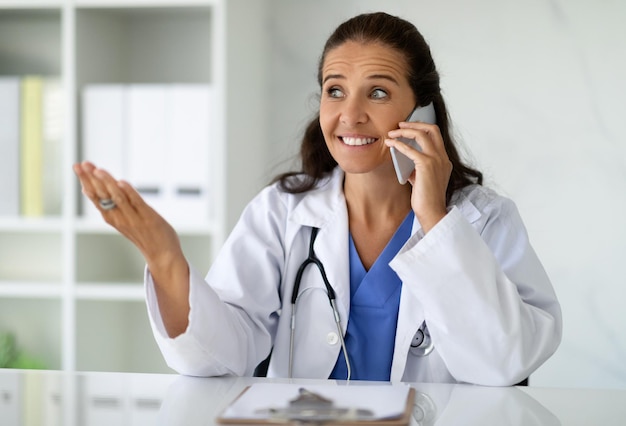 Smiling middle aged woman therapist in uniform talking by phone