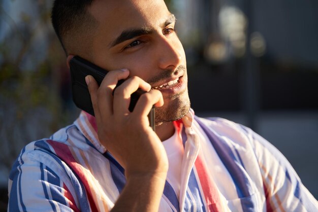 Foto sorridente uomo mediorientale che parla al cellulare per strada, fuoco selettivo. concetto di tecnologia